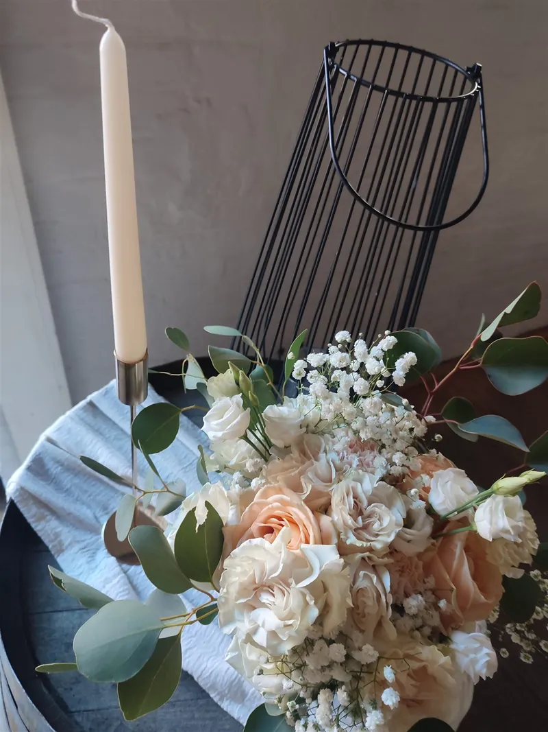 Kerze und Eukalyptus neben cremefarbenen Rosen, im Hintergrund ein schwarzer Drahtkorb
