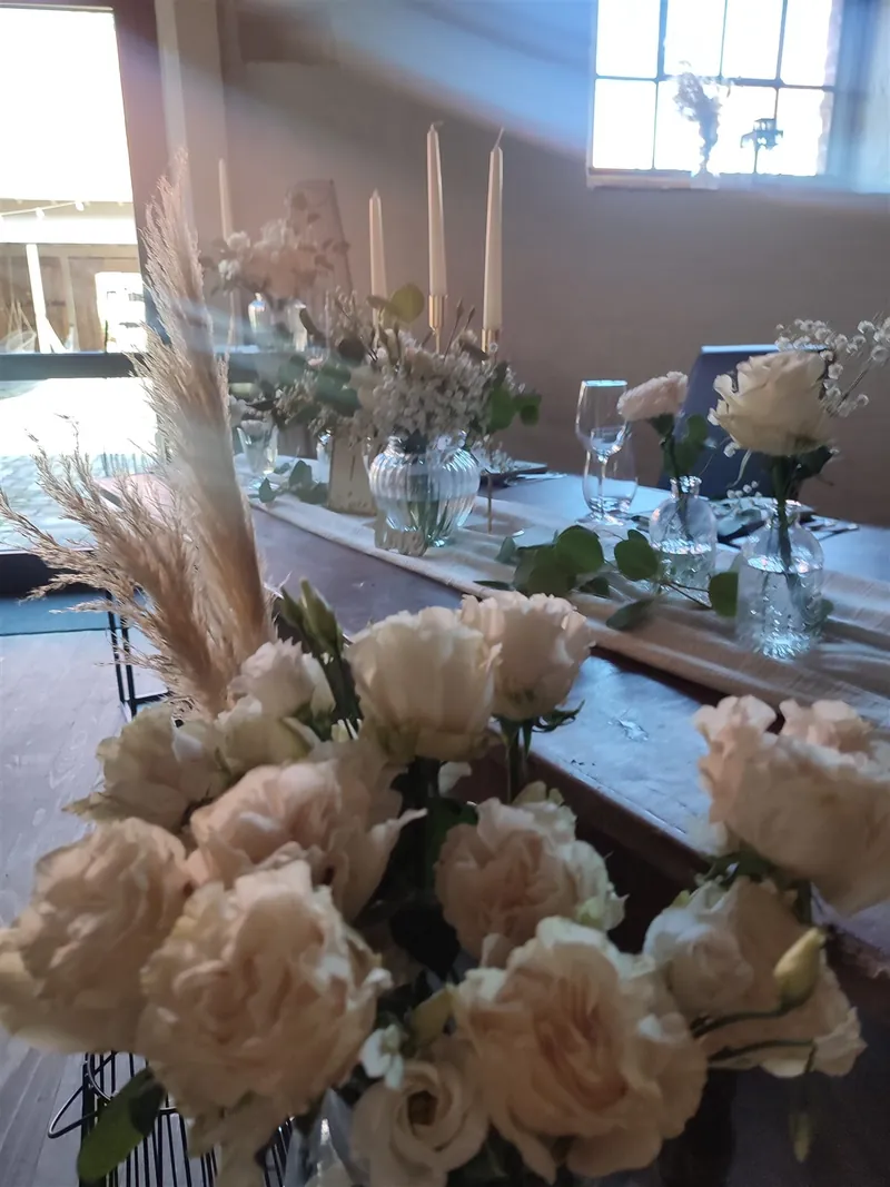 Lange Hochzeitstafel mit Pampasgras, Rosen und Kerzenlicht in der Scheune