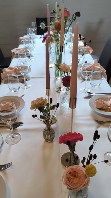 Festlich gedeckte Tafel mit Apricot-Servietten, Stabkerzen und kleinen Blumenvasen