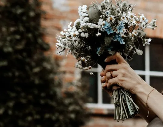 Wildblumenstrauß mit Disteln, Margeriten und blauen Blüten, in der Hand gehalten